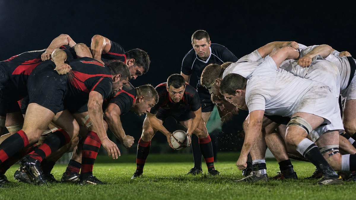 Five-player 10s rugby scrum with two props, a hooker and two locks engaging under floodlights