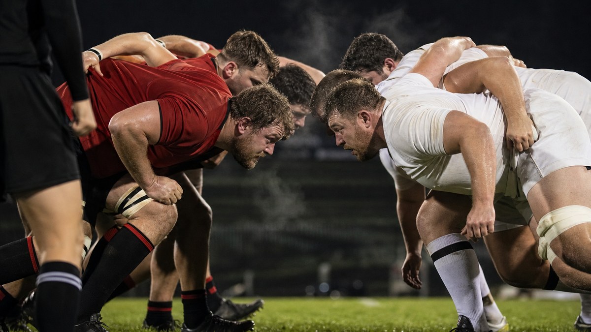 Five-player rugby scrum engaging on a floodlit pitch during a 10s rugby match